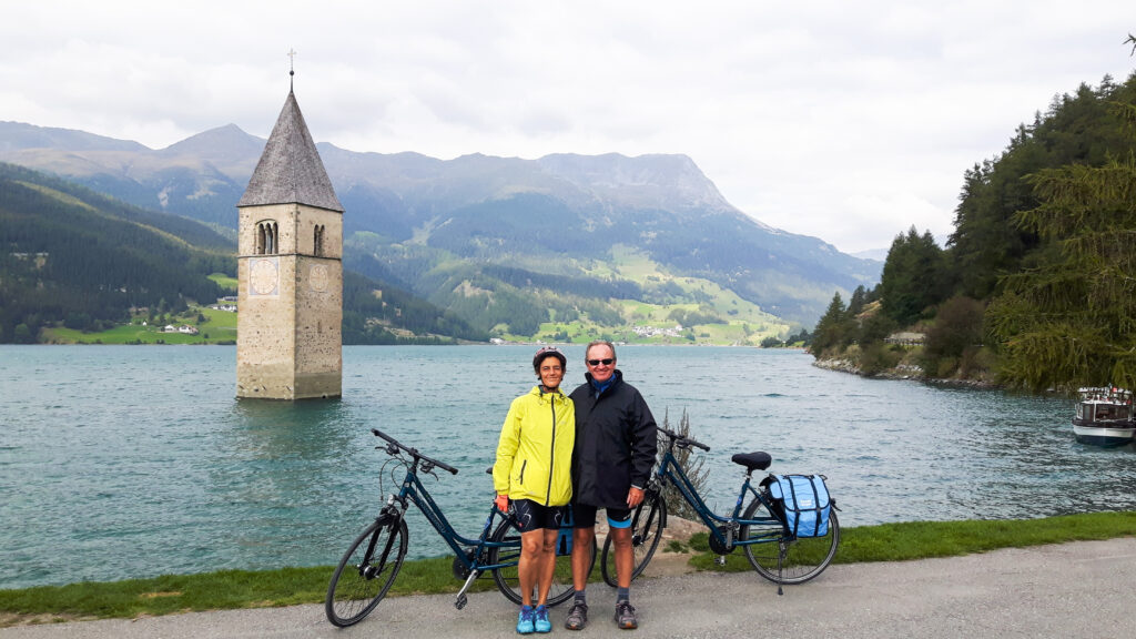 Radfahrer neben dem versunkenen Glockenturm im Reschensee, Südtirol, Italien.